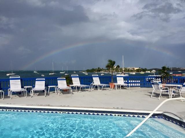 Hotel pool with white beach chairs under a dark sky with a rainbow