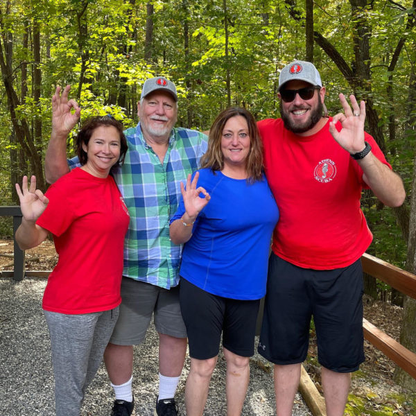 Four adults, two wearing hats with the Athens Scuba logo, posing in the woods