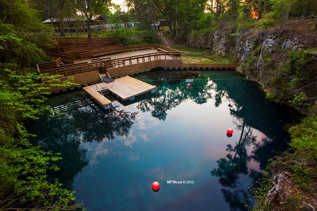 A wooden deck and dock on a blue grotto surrounded by trees