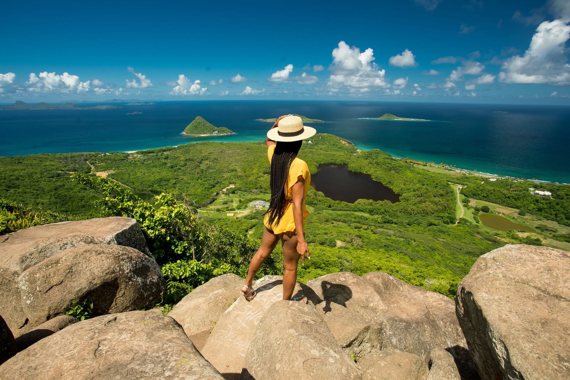 Woman with a hat standing on rocks looking out over islands