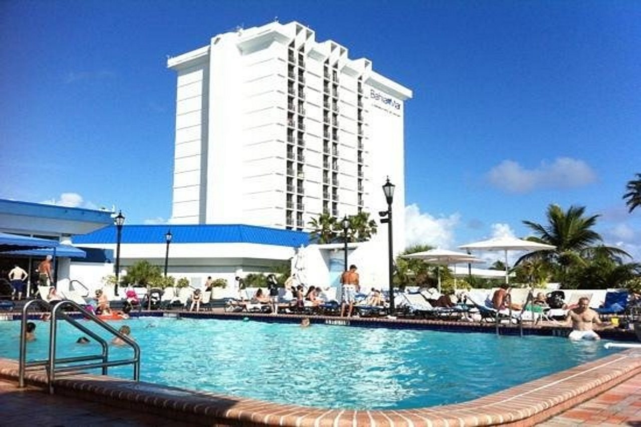 A pool filled with people lounging and a tall white hotel in the background